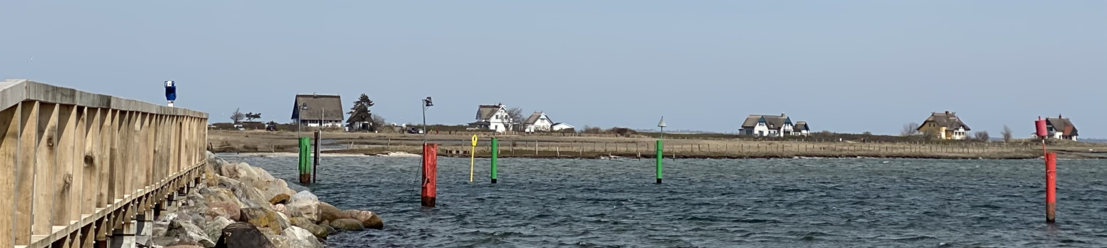 rote und grüne Markierungen in einem Fahrwasser vor einer besiedelten Küste