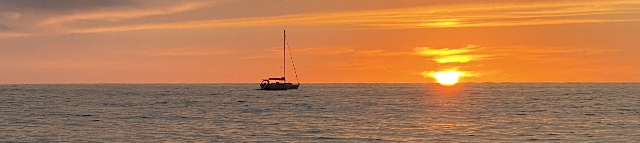 Ein einsames Segelboot liegt auf ruhigem offenem Meer bei orangefarbigem Sonnenuntergang